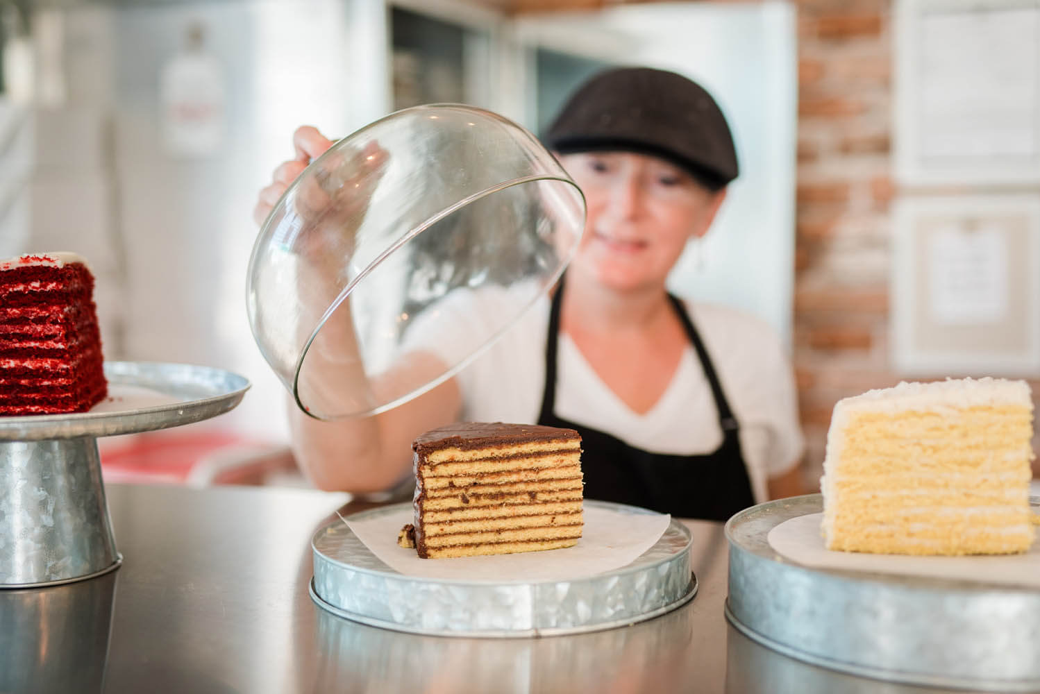 Female pastry chef in front of three pieces of cake placed on cake holder