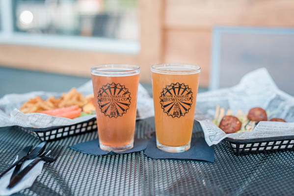 Close-up view of two glasses of beer and two plates of French fries and sausages on a restaurant table outside