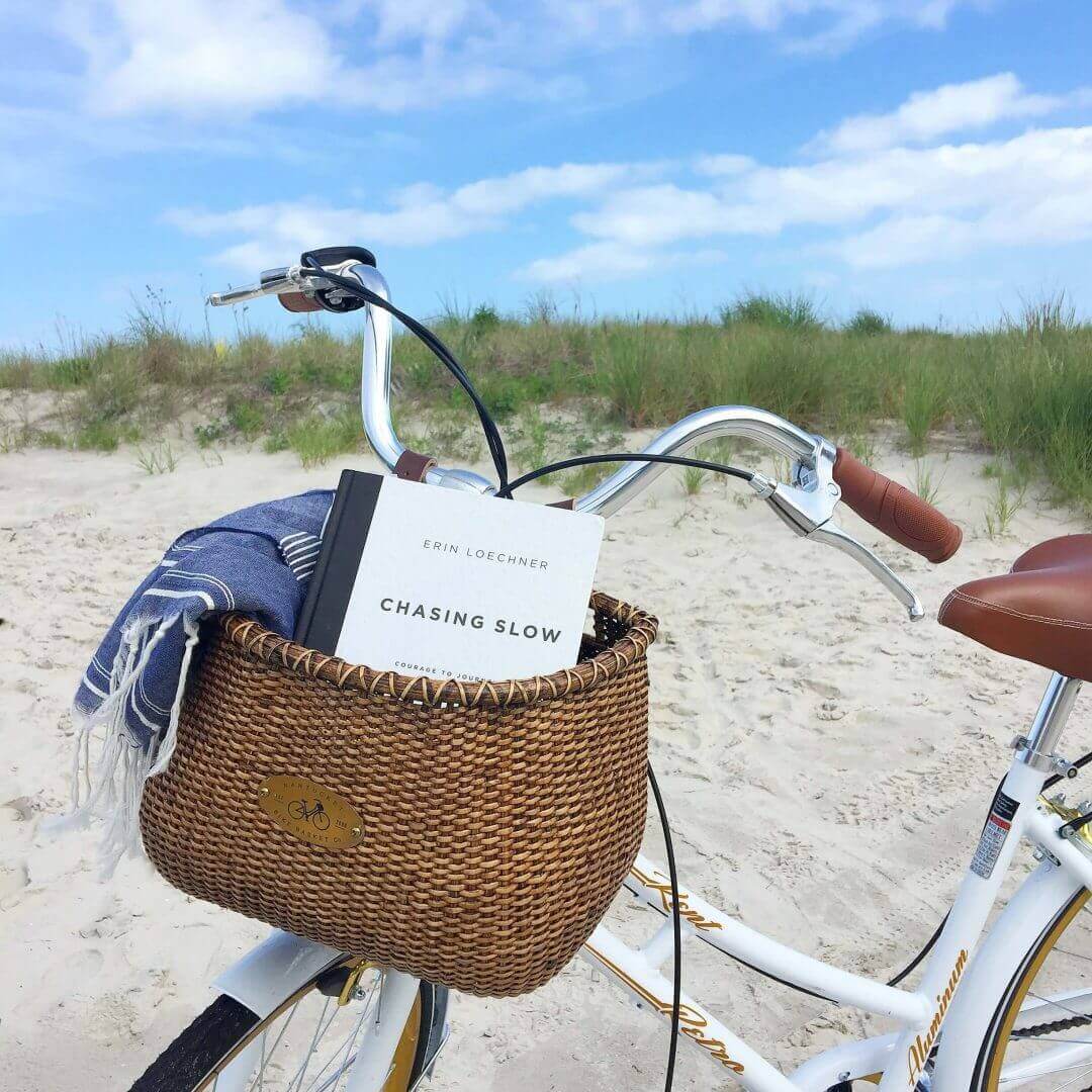 Close-up view of a bicycle basket with a book and a blanket inside, on the beach